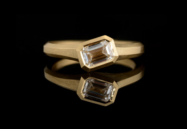 Bespoke Arris carved yellow gold engagement ring with emerald cut white diamond
